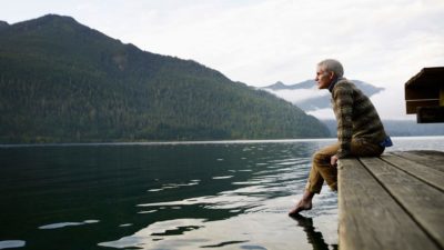man sits on the dock enjoying the quite of the lake in the mountains