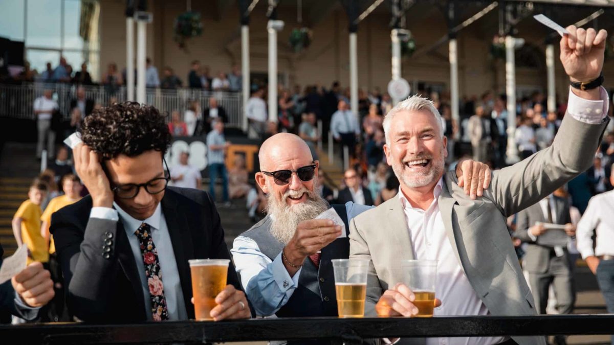 Two men celebrate while another holds his head in his hands, after watching the race.