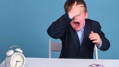 Young boy cries and covers eyes with torn money on table