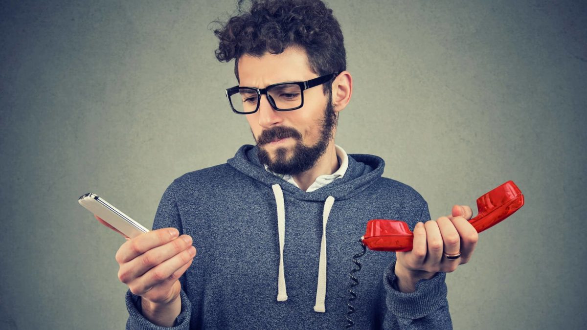 A man in a sweatshirt holds two different phones to compare telco services.