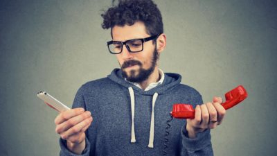 A man in a sweatshirt holds two different phones to compare telco services.