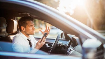 Driver sitting in car, holding phone and looking frustrated