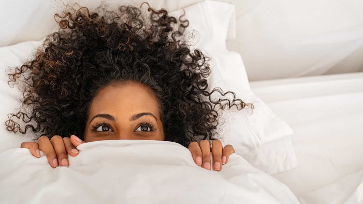 A happy woman peaks out from under her bed sheets