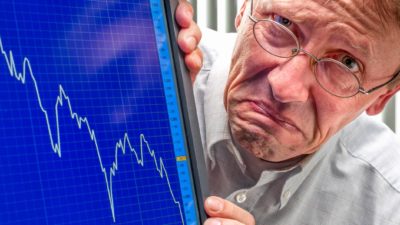 man grimaces next to falling stock graph