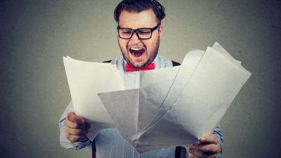 A dismayed businessman holds up a stack of new rules and regulations