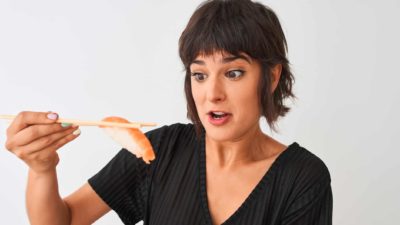 A surprised woman holds a piece of salmon with chopsticks