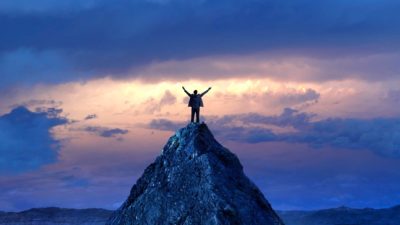a person stands arms outstretched on the top of a mountain with a beautiful sunrise in the sky