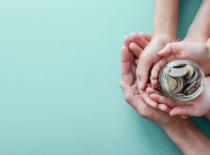 A parent's hands cup a child's as they hold a small jar of money.