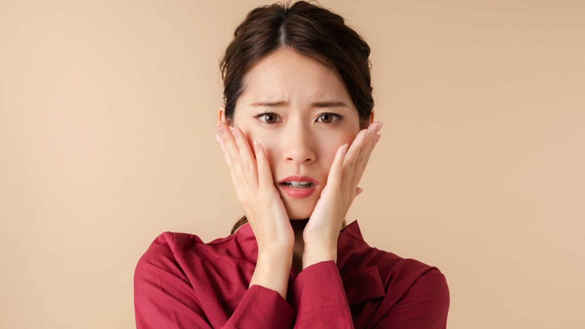 A woman holds her hands to her face in shock and fear with a worried expression on her face as many ASX 200 shares hit 52-week lows today