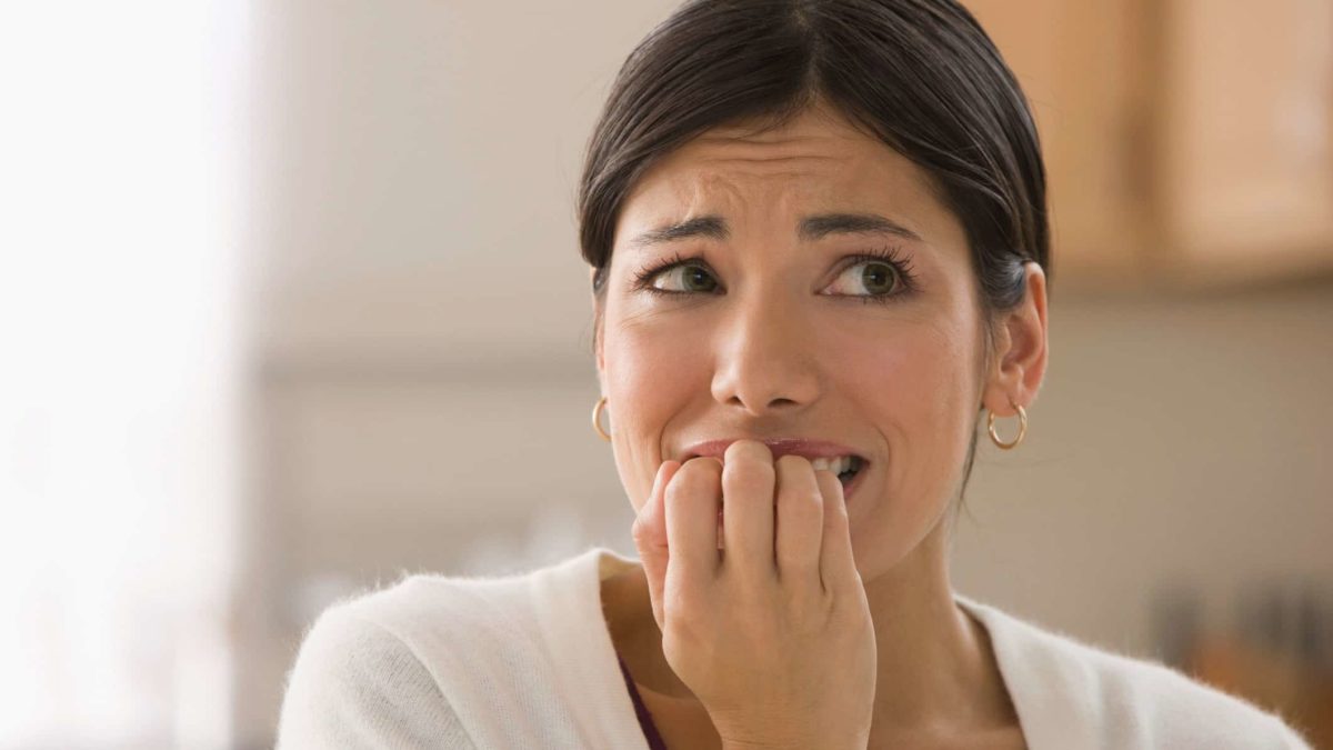 a woman bites on her fingernails in an anguished pose of fear and dread.