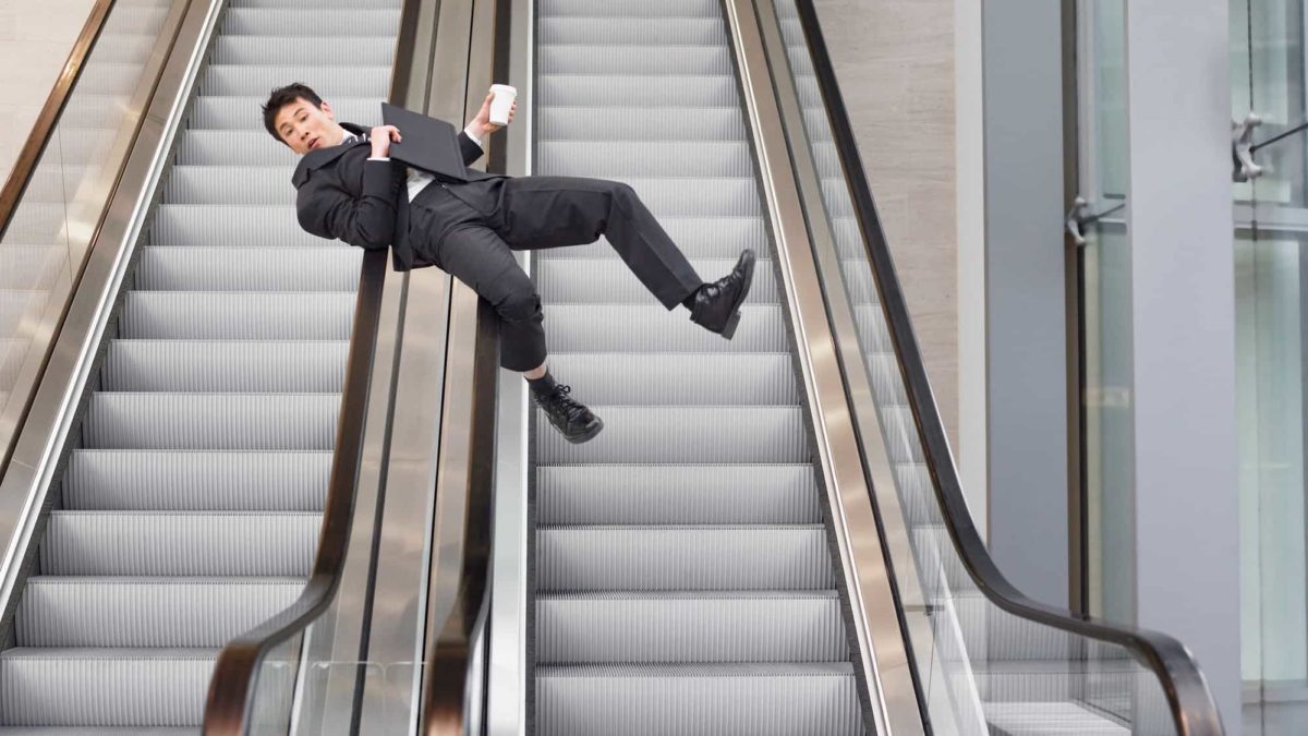 A man in a business suit slides down the handrails of a bank of steel escalators, clutching his documents and telephone.