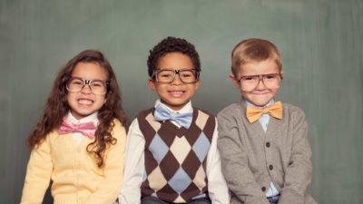 a group of smart looking kids, wearing formal clothes and all with spectacles, sit in a line and smile charmingly.