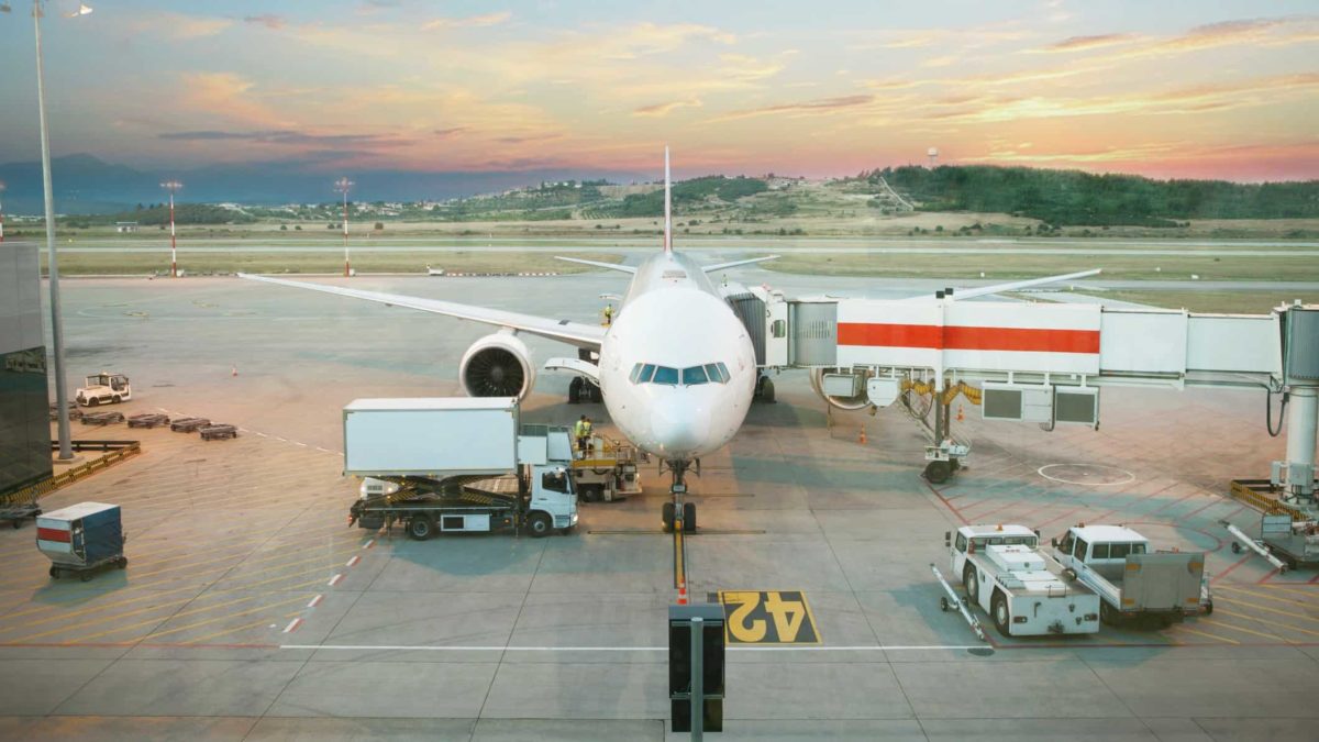 a passenger plane is on the tarmac with passenger shute attached with a view of the surrounding land and sunset in the background.