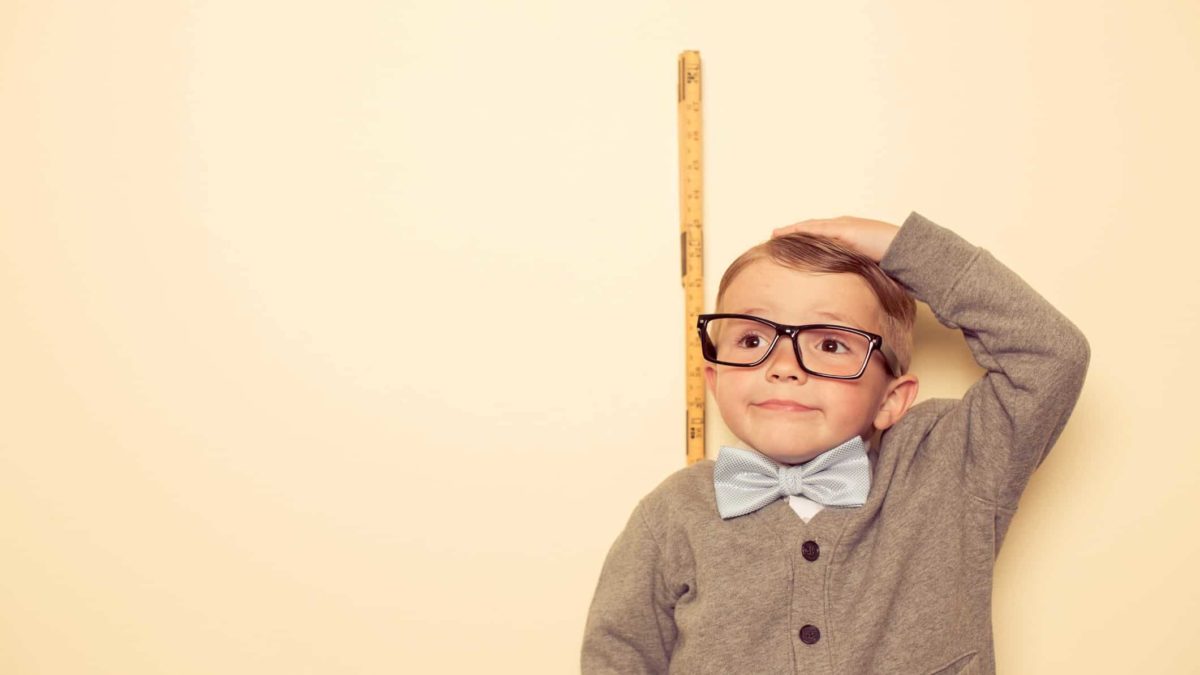 A little boy measures himself against a ruler and comes up short.