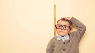 A little boy measures himself against a ruler and comes up short.
