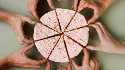 Lots of hands reach in to take a share of a birthday cake.