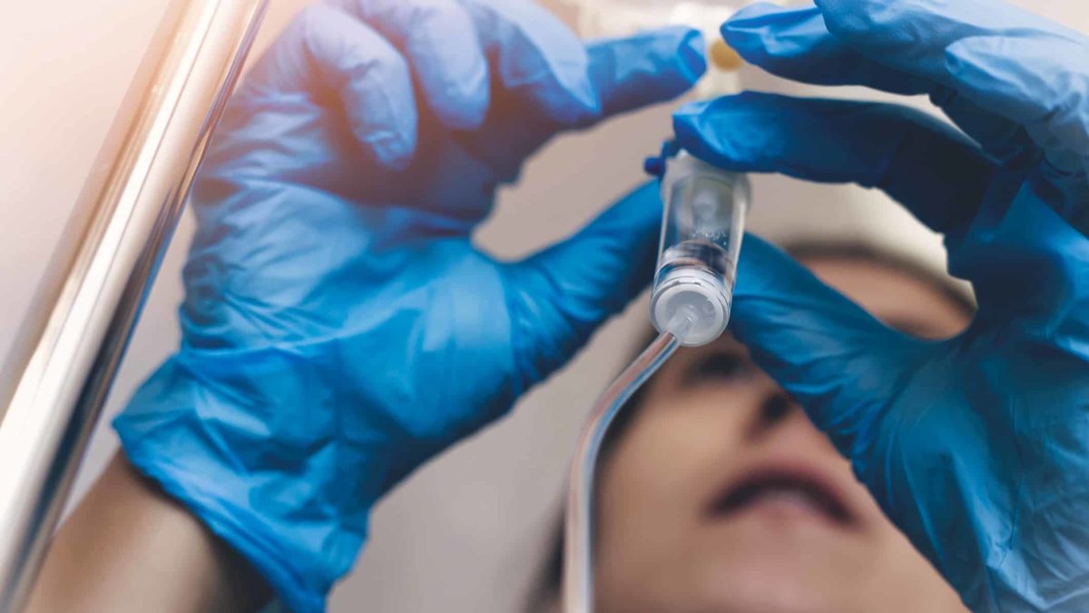 A health worker wearing disposable gloves holds a vial, treating a patient.
