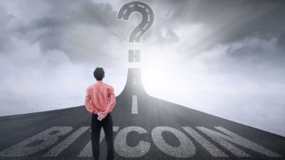 A man stands on a road marked Bitcoin with a questionmark ahead.