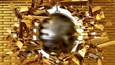 A wrecking ball swings through a wall of gold bricks, sending them flying.