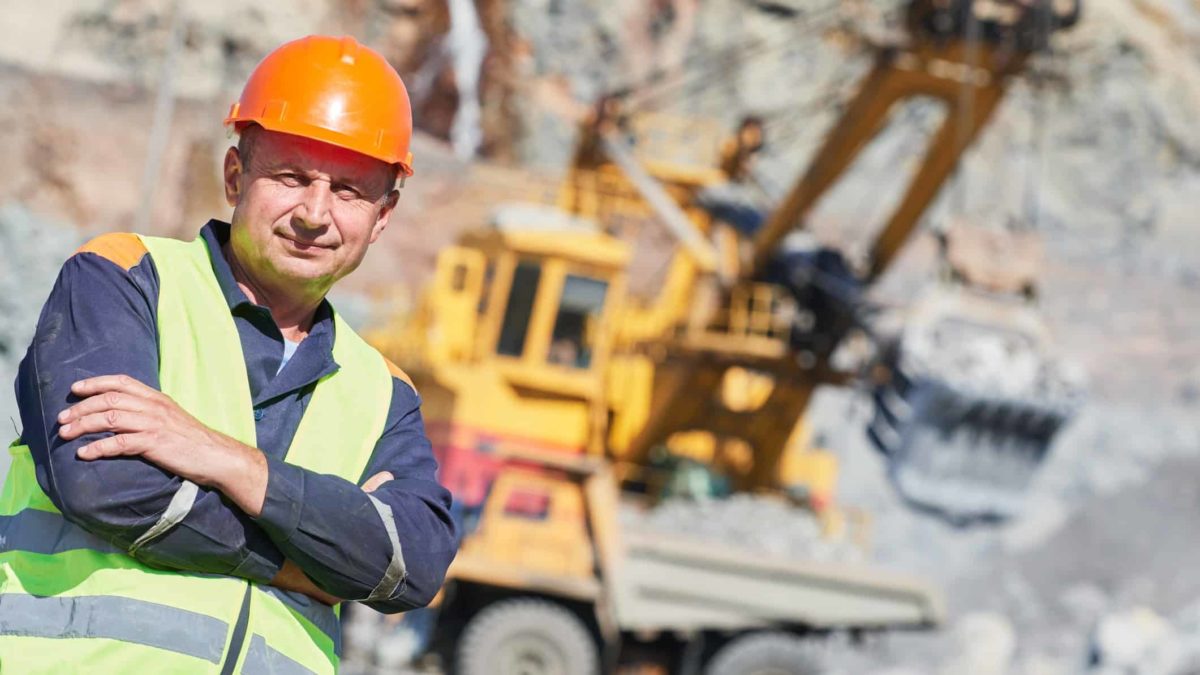 A miner stands in front oh an excavator at a mine site