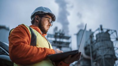 A worker with a clipboard stands in front of a nuclear energy facility