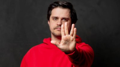 Man in red jumper holds hand out in a vulcan salute.