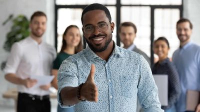 A man standing in front of co-workers extends his hand in welcome