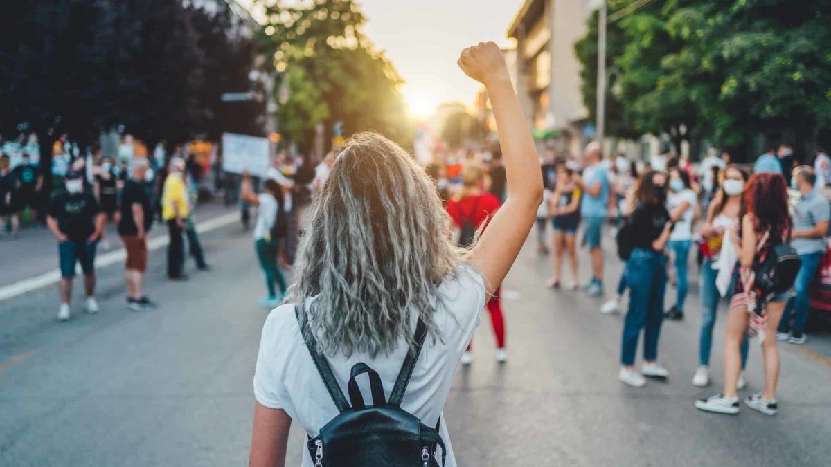 A woman stands among activists in the street with her fist in the air.