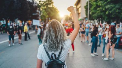 A woman stands among activists in the street with her fist in the air.