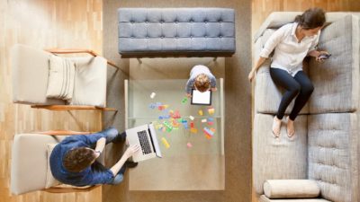 A family sits around the living room, each on a different device.