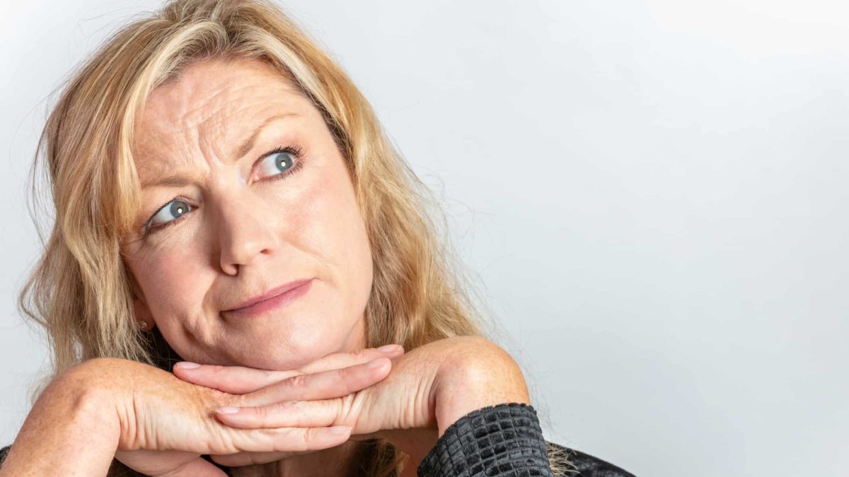 A woman frowns slightly and looks with her eyes to the side while holding her hands under her chin as she contemplates whether now is the time to buy the dip in ASX 200 shares