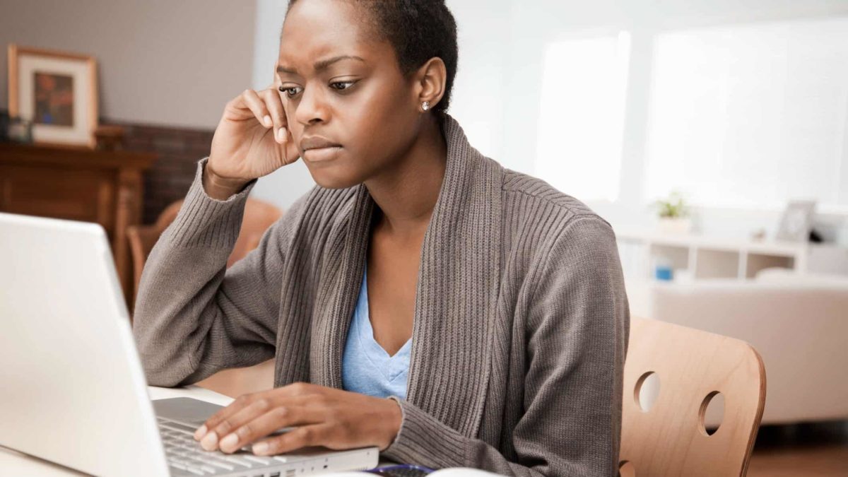 a woman sits with a concerned look on her face at her computer in an home office environment.