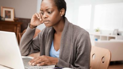 a woman sits with a concerned look on her face at her computer in an home office environment.