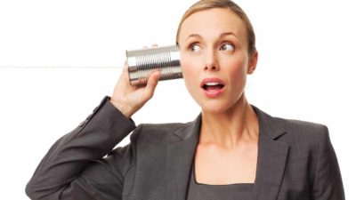 a woman in a business suit looks wide eyed and interested as she holds a tin can with string to hear ear listening to some news.