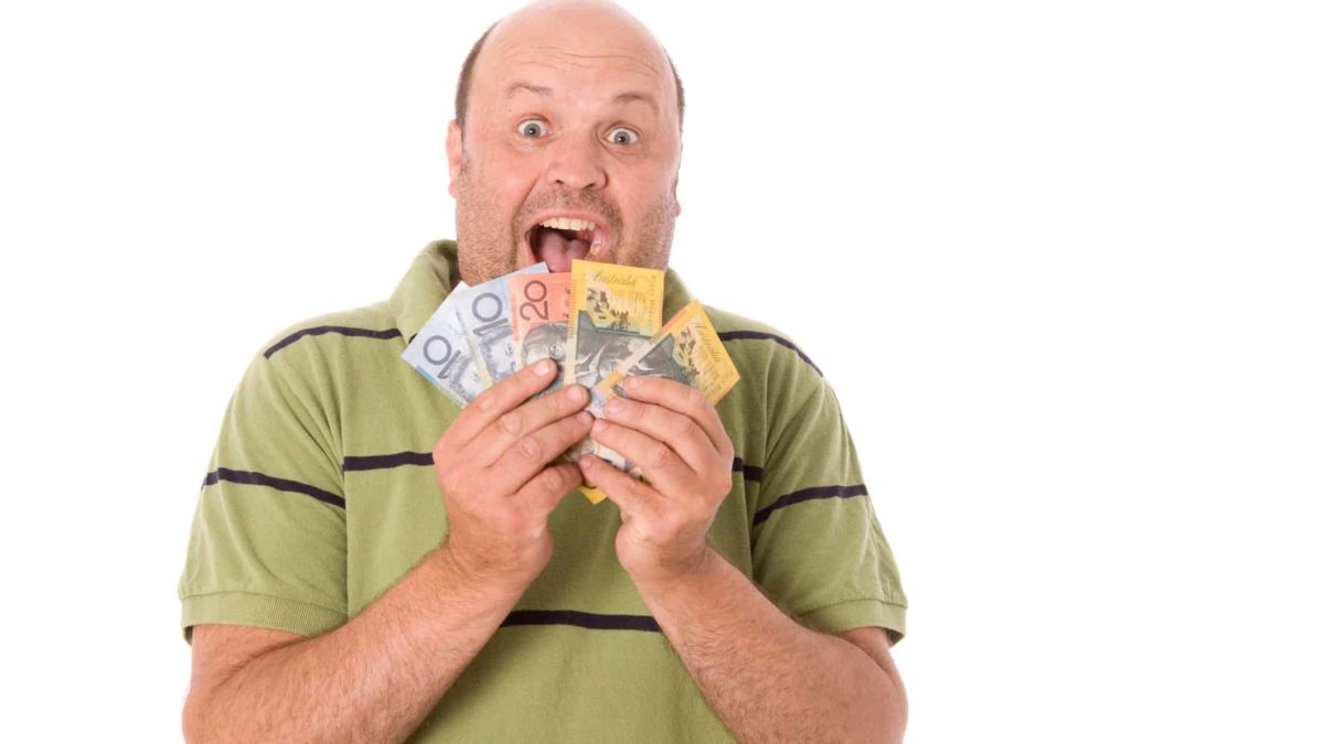 a man wearing casual clothes fans a selection of Australian banknotes over his chin with an excited, widemouthed expression on his face.