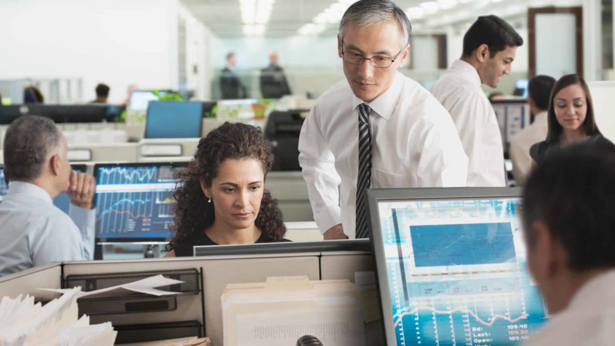 A group of market analysts sit and stand around their computers in an open-plan office environment. The central figures are deep in thought about Megaport's recent earnings release