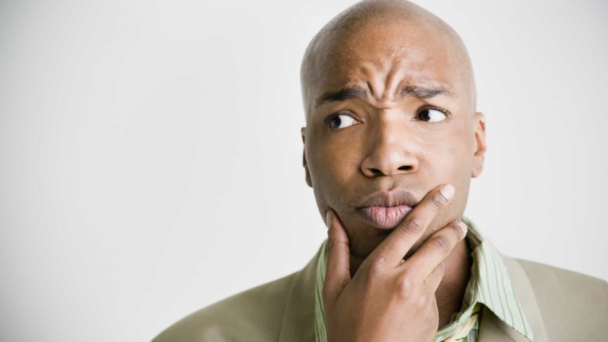 a man holds his hand to his chin with a furrowed brow, making an expression of puzzlement or confusion.