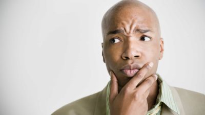 a man holds his hand to his chin with a furrowed brow, making an expression of puzzlement or confusion.