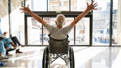 A man in a wheelchair stretches both arms into the air in success.