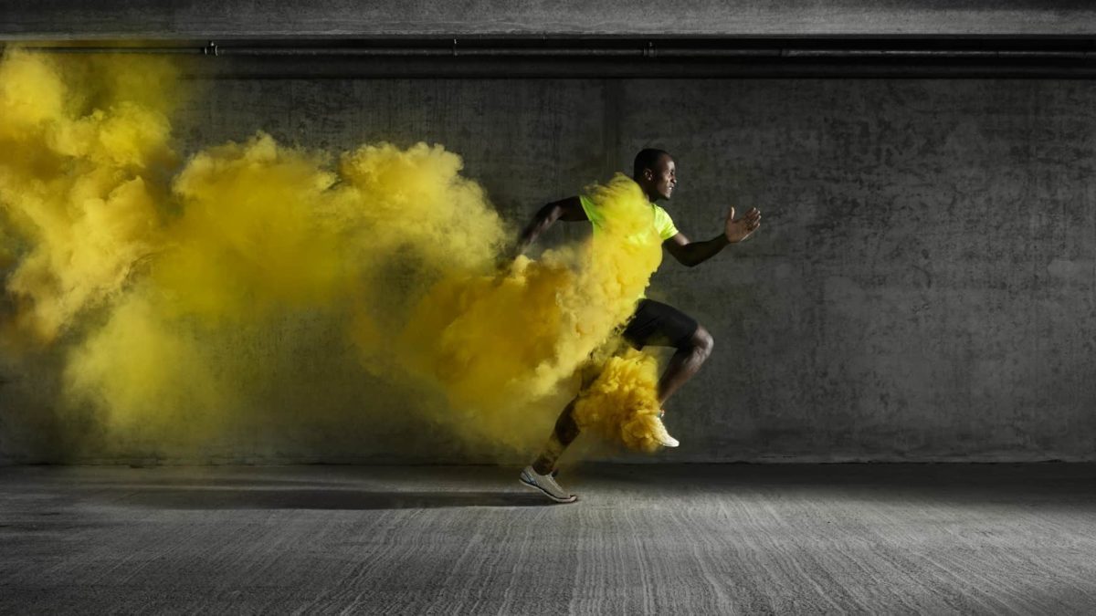 An athlete runs fast with a trail of yellow smoke billowing out behind him.