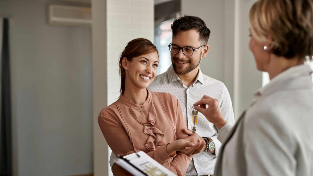 Young couple smiling as they accept keys from their real estate agent for their new home