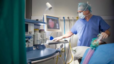 An anaesthetist in an operating theatre looks at a computer screen while patient sleeps