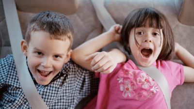 A boy and girl cheer with seatbelts on in car.