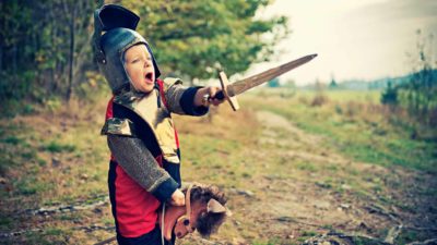 A boy dressed as a knight charges ahead on his toy horse