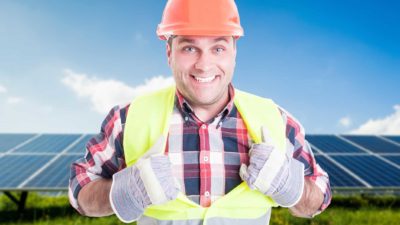 Thumbs up for clean energy. A construction worker or miner in front of solar panels.