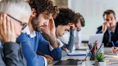 Group of entrepreneurs feeling frustrated during a meeting in the office. Focus is on man with headache.