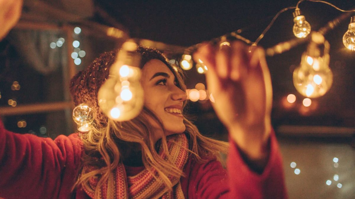 Happy woman stringing lights at an outside party.