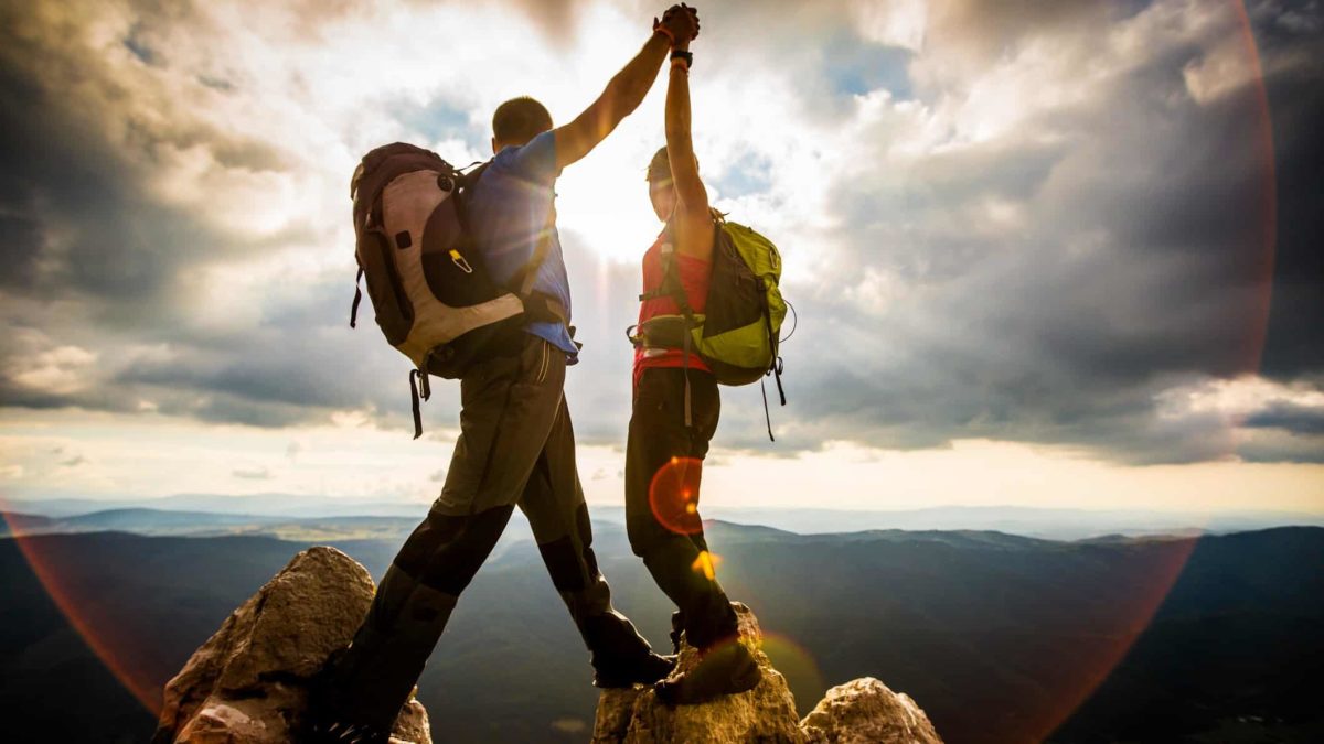 Two hikers high five each other having climbed to the top pinnacle of the mountain.