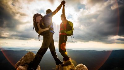 Two hikers high five each other having climbed to the top pinnacle of the mountain.