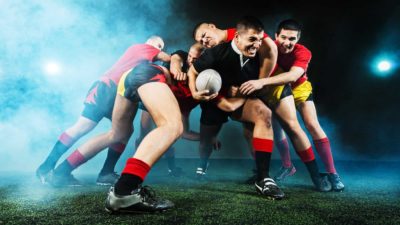 Rugby player runs with the ball as four tacklers try to stop him.